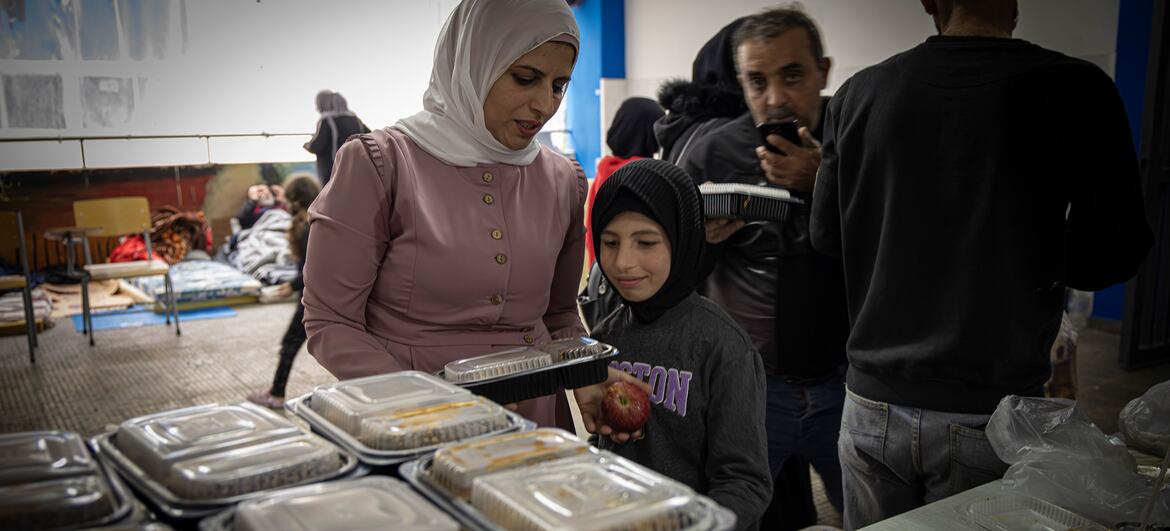 A woman and a young girl receive food containers at a distribution center in a Beirut school. Other displaced people are seen in the background.