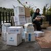 Une femme déplacée portant un hijab et tenant un bébé est assise à côté d'une grande pile de boîtes d'aide alimentaire de l'UNICEF et du PAM au Liban.