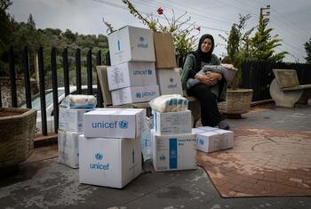 Une femme déplacée portant un hijab et tenant un bébé est assise à côté d'une grande pile de boîtes d'aide alimentaire de l'UNICEF et du PAM au Liban.