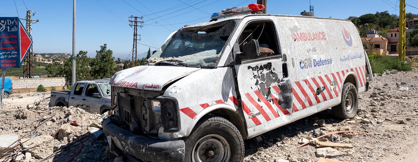 Une ambulance blanche gravement endommagée, aux vitres brisées et percée de balles, est stationnée au milieu des décombres dans une rue de Tebnine, au Liban, illustrant l'impact du conflit sur les services d'urgence.