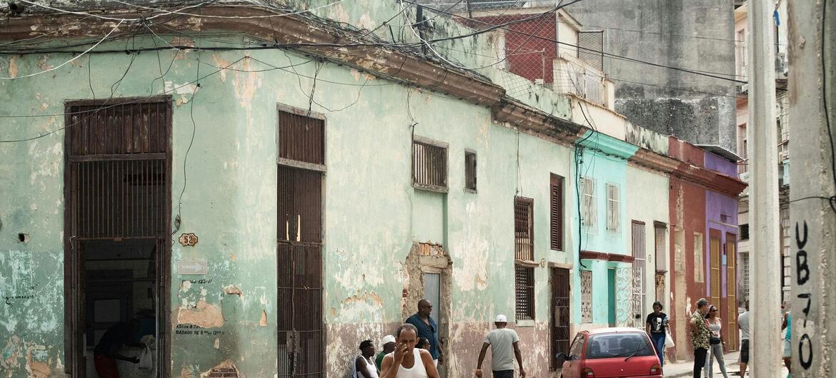Une scène de rue dans la vieille Havane, à Cuba, montrant des bâtiments délabrés à la peinture écaillée et plusieurs hommes marchant sur le trottoir.