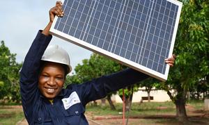 A teenage woman in Côte d'Ivoire holds up a solar panel. Boosting renewable energy is a key part of the climate action agenda.