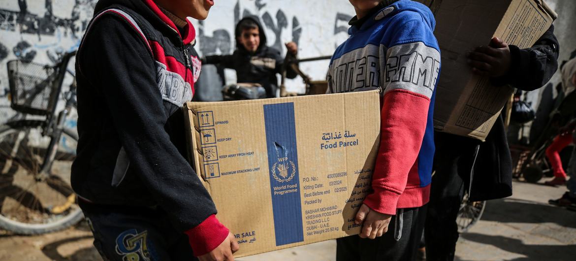 شخصان يحملان طردا غذائيا مقدما من برنامج الأغذية العالمي، في مخيم النصيرات - وسط قطاع غزة.