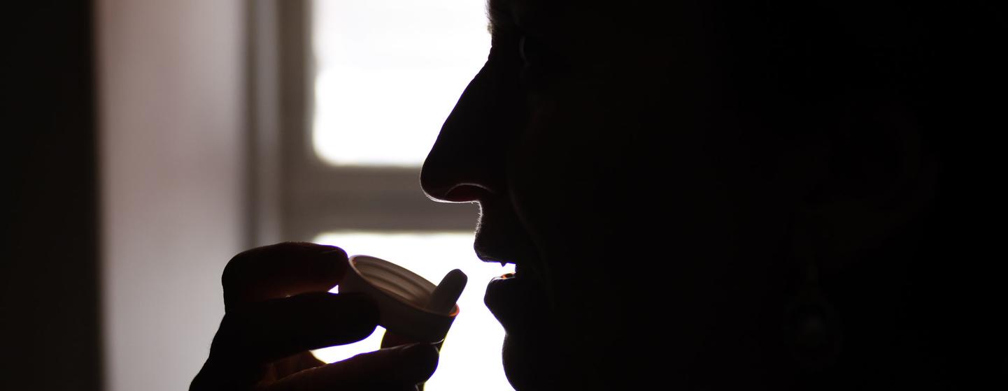 Mulher tomando medicação em silhueta contra uma janela.