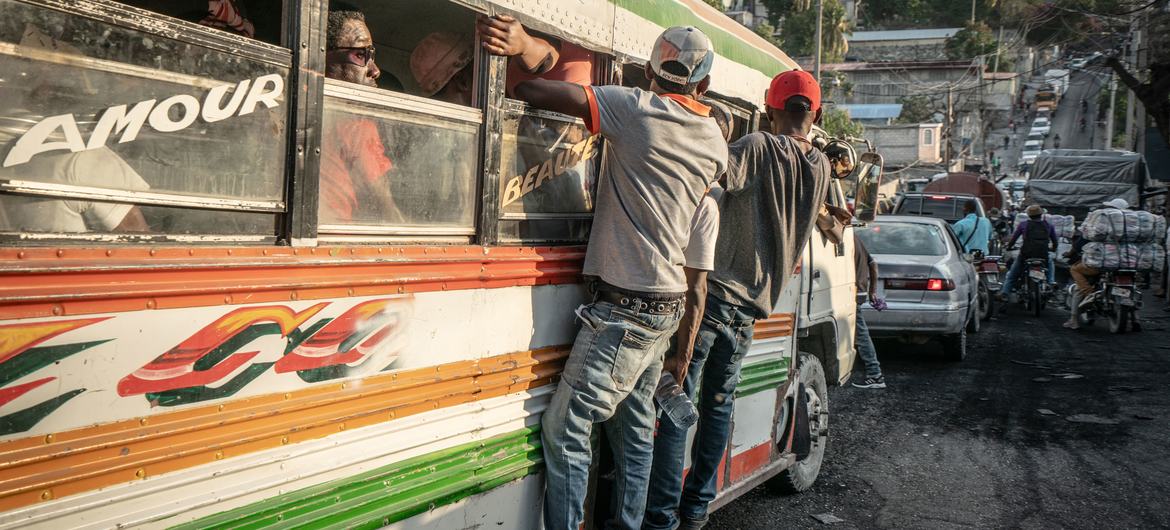 Passageiros agarrados à parte externa de um ônibus nas ruas de Porto Príncipe