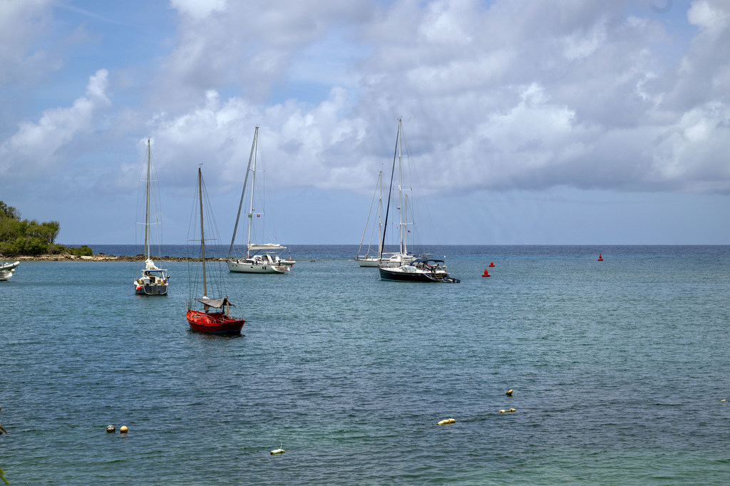 Varios veleros fondeados en un tranquilo puerto deportivo en St. John's, Antigua y Barbuda, bajo un cielo parcialmente nublado.