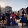 تجمع النساء والأطفال الفلسطينيات المياه في حاويات وسط أنقاض المباني المدمرة في دير البلح بغزة.