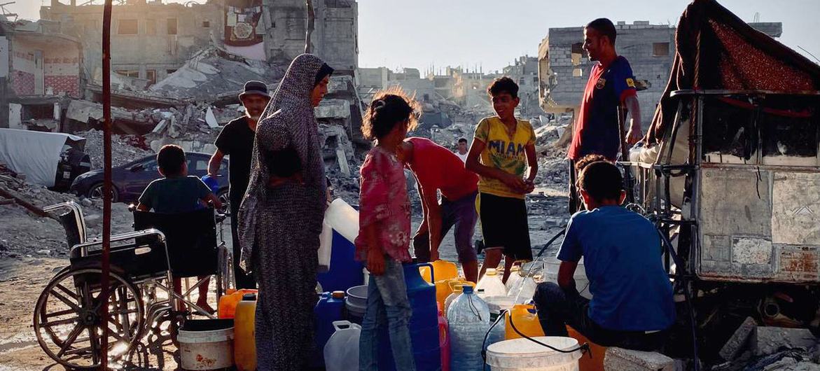 تجمع النساء والأطفال الفلسطينيات المياه في حاويات وسط أنقاض المباني المدمرة في دير البلح بغزة.