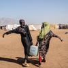 Deux jeunes femmes transportent de l'eau sur un site pour personnes déplacées dans l'est du Soudan.