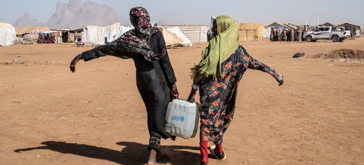 Deux jeunes femmes transportent de l'eau sur un site pour personnes déplacées dans l'est du Soudan.