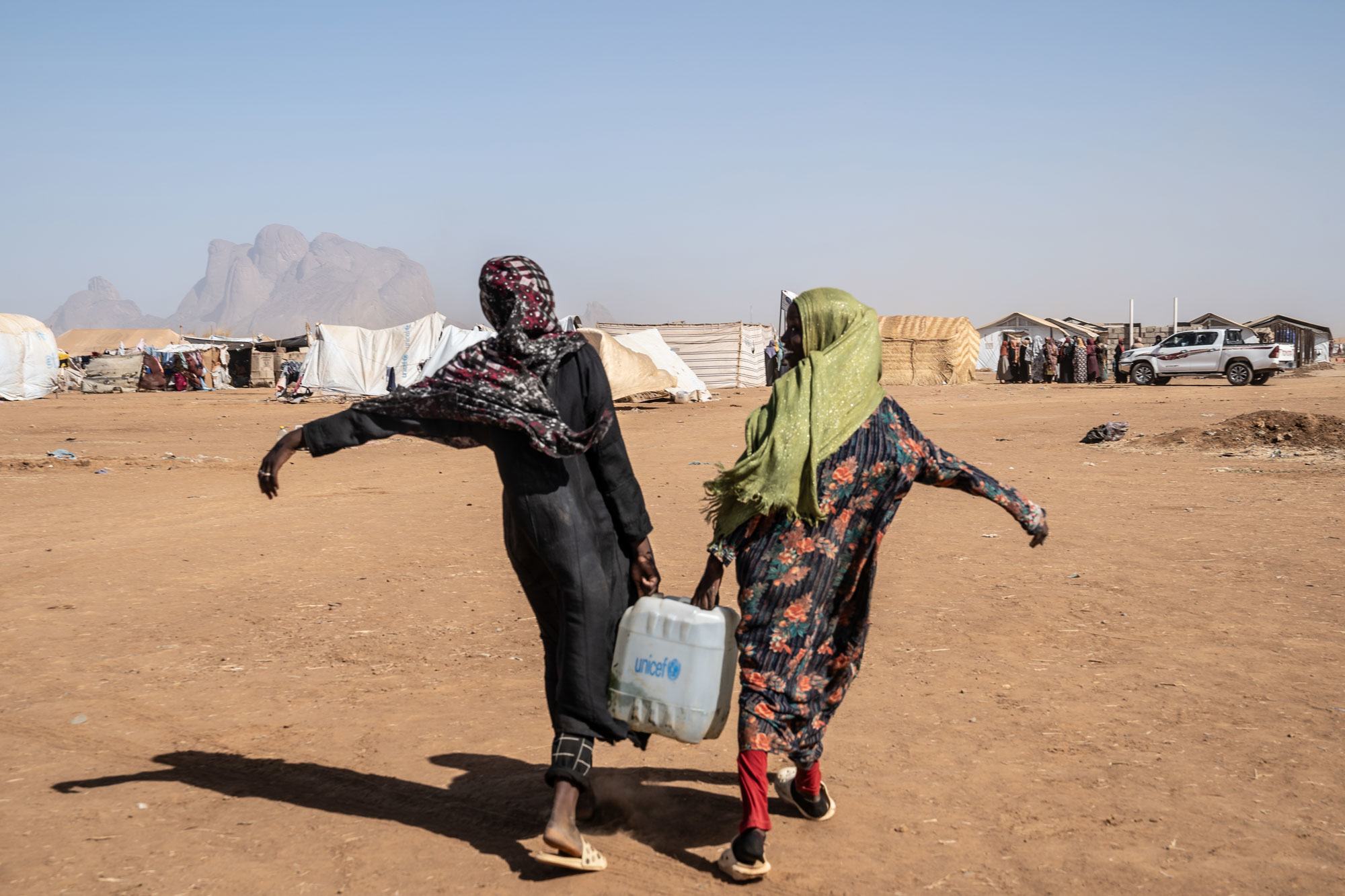 Two young women carry water at a site for displaced people in eastern Sudan. Two young women carry water at a site for displaced people in eastern Sudan.