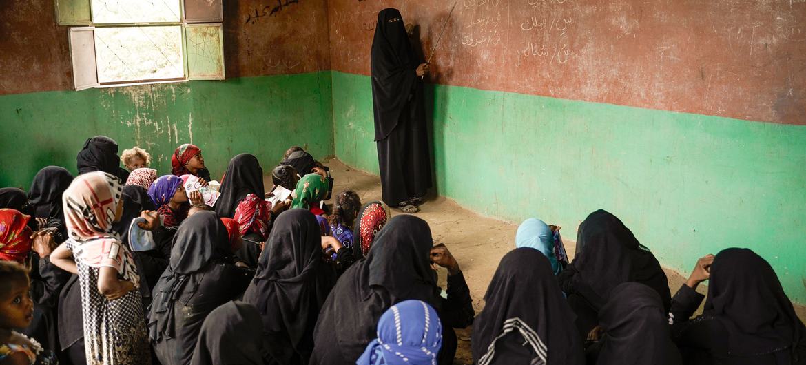 A female teacher in Yemen writes on a chalkboard in a classroom filled with young female students.