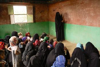 A female teacher in Yemen writes on a chalkboard in a classroom filled with young female students.