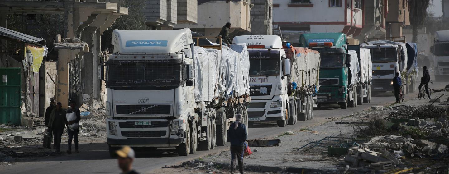 Un convoi de camions transportant de l'aide humanitaire entre dans la bande de Gaza par le passage de Kerem Shalom, en passant devant des bâtiments endommagés et des décombres.