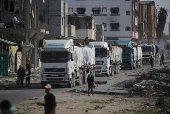 Un convoi de camions transportant de l'aide humanitaire entre dans la bande de Gaza par le passage de Kerem Shalom, en passant devant des bâtiments endommagés et des décombres.