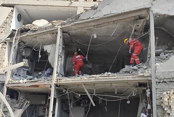 Deux sauveteurs de la Croix-Rouge rouge iranienne en uniforme orange fouillent les décombres à l'intérieur d'un bâtiment endommagé.