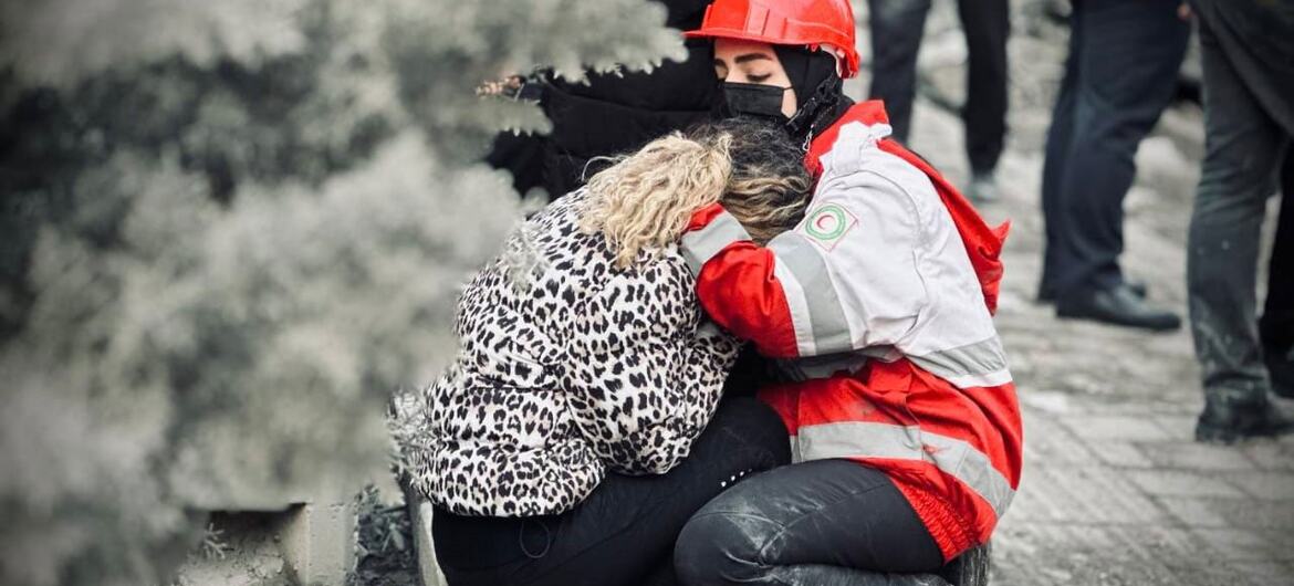 Um voluntário da Sociedade do Crescente Vermelho do Irã, usando um capacete vermelho e uma máscara facial, consola uma mulher angustiada em meio aos escombros em Teerã, no Irã.