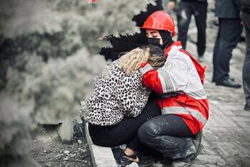 Un voluntario de la Sociedad de la Media Luna Roja de Irán, que lleva un casco rojo y una mascarilla facial, consuela a una mujer angustiada en medio de los escombros en Teherán, Irán.