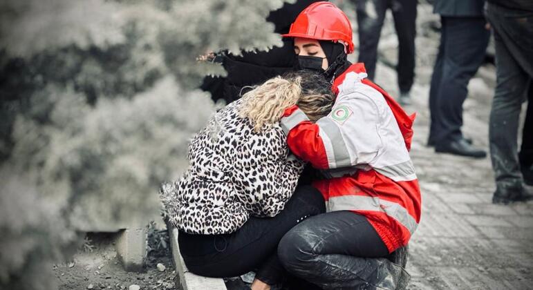 Un voluntario de la Sociedad de la Media Luna Roja de Irán, que lleva un casco rojo y una mascarilla facial, consuela a una mujer angustiada en medio de los escombros en Teherán, Irán.