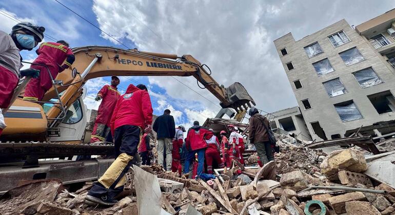Les sauveteurs de la Société du Croissant-Rouge iranien, vêtus d'uniformes rouges, travaillent au milieu des décombres et d'un bâtiment endommagé, à côté d'une pelleteuse, lors d'une opération de secours à Téhéran, en Iran.