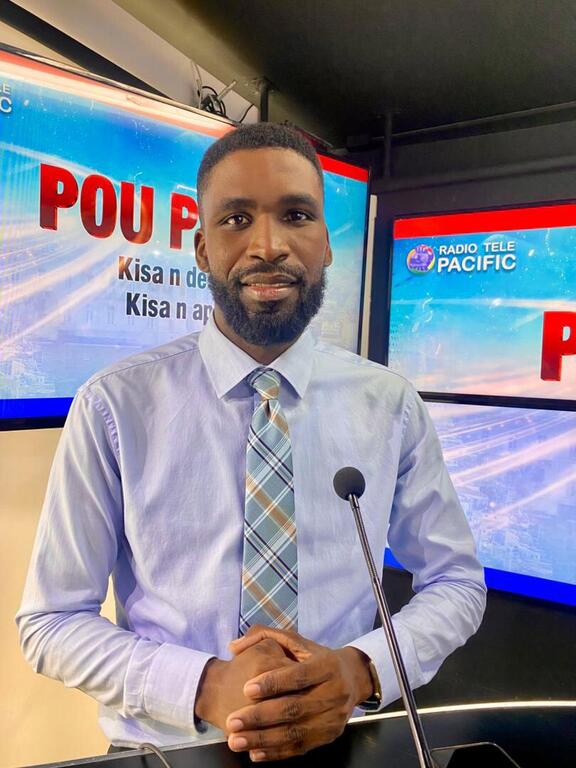 Oberde Charles, Newsroom Manager at Pacific TV and Editor at Le National newspaper, stands in a television studio with microphones and screens displaying 'Radio Tele Pacific' and 'POU P'.