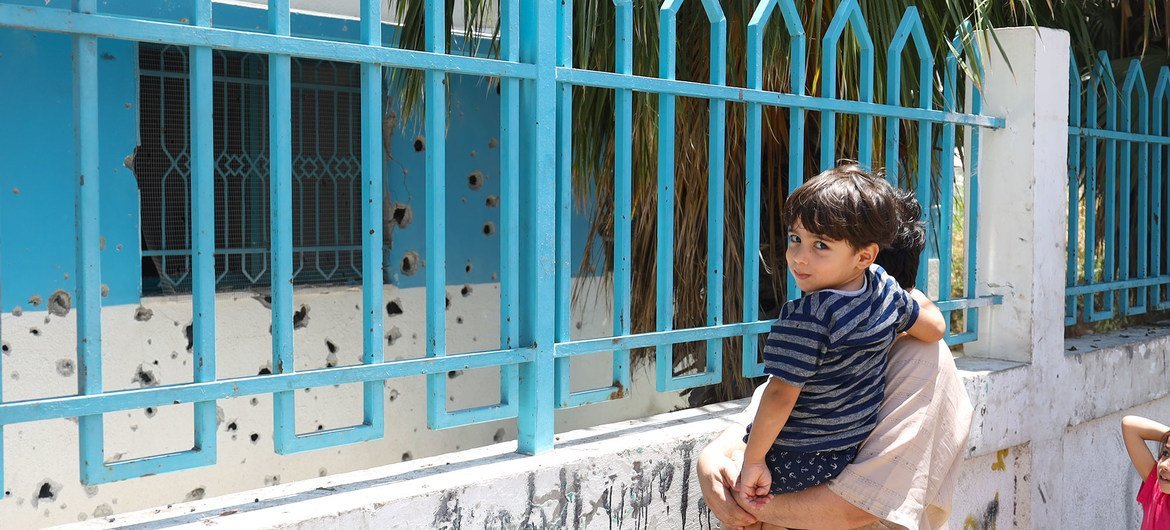 A Palestinian man holds his son in front of a clinic in Al-Daraj, Gaza which was bombed in May 2021.