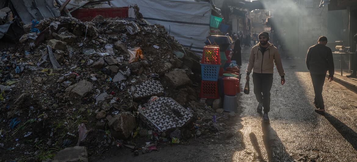 Un homme se promène dans une rue ravagée par la guerre à Gaza, en passant par des tas de décombres et de décombres, alors que la fumée monte d'un incendie voisin.