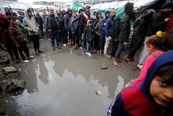 Palestinos fazem fila para conseguir comida sob chuva em um abrigo em Deir Al-Balah, Gaza