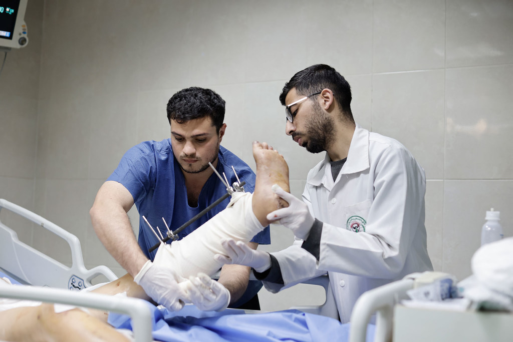 Wataalamu wawili wa matibabu wa Kipalestina wakimtibu mguu wa mtu aliyejeruhiwa katika kitanda cha hospitali katika Kituo cha Matibabu cha Nasser huko Khan Younis.