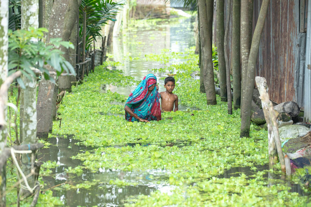 A woman and child wads through floodwater in Kurigram, Bangladesh .