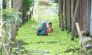 A woman and child wads through floodwater in Kurigram, Bangladesh .