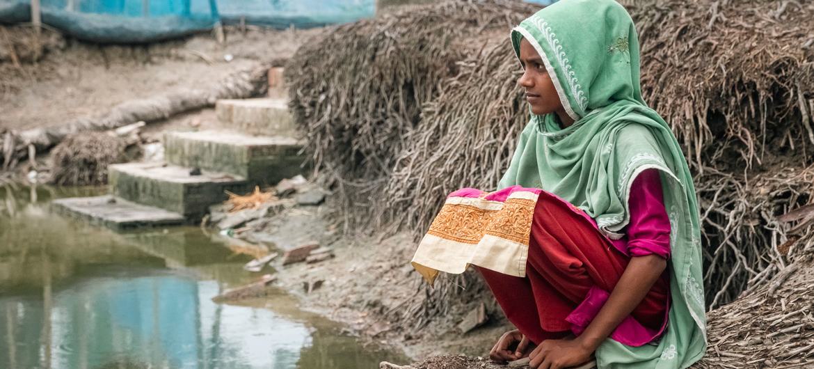 Shiuli Sultana, 13, sits on the exposed roots of a dead tree beside stagnant water in her flooded home village of Sreeula, Southern Bangladesh.