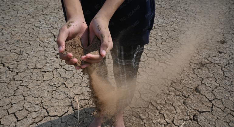 Una persona permanece descalza sobre tierra agrietada y reseca, sosteniendo tierra seca entre sus manos.