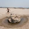 Un niño pequeño corre hacia una gran roca con un pequeño charco de agua en un paisaje seco y árido en el distrito de Ban Phai, provincia de Khon Kaen, Tailandia.