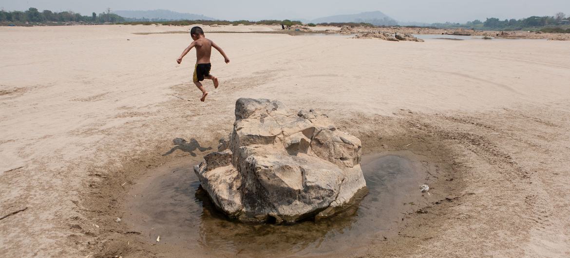 Un niño pequeño corre hacia una gran roca con un pequeño charco de agua en un paisaje seco y árido en el distrito de Ban Phai, provincia de Khon Kaen, Tailandia.
