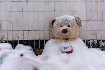 Um urso de peluche coberto de neve está sentado fora de um prédio residencial em Kiev, na Ucrânia, durante uma interrupção de energia e aquecimento de inverno causada por ataques a infraestruturas críticas.