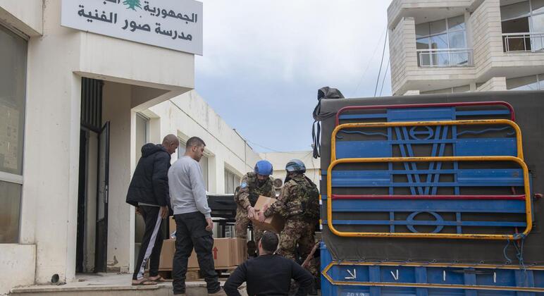 Os peacekeepers italianos da UNIFIL em capacetes azuis descarregam caixas de ajuda alimentar de um caminhão militar para pessoas deslocadas em Tiro, Líbano.