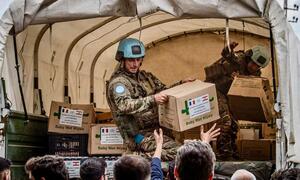 UNIFIL peacekeepers in camouflage uniforms and blue helmets unload humanitarian aid supplies, including food and medicine boxes labeled 'Baby Wet Wipes' and marked with UN and French flags, from a military truck to civilians in Lebanon.