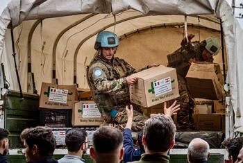 Les forces de maintien de la paix de l'UNIFIL, vêtues d'uniformes de camouflage et de casques bleus, déchargent des fournitures d'aide humanitaire, y compris des boîtes de nourriture et de médicaments étiquetées "Baby Wet Wipes" et marquées de drapeaux de l'ONU et de la France, à partir d'un camion militaire vers des civils au Liban.