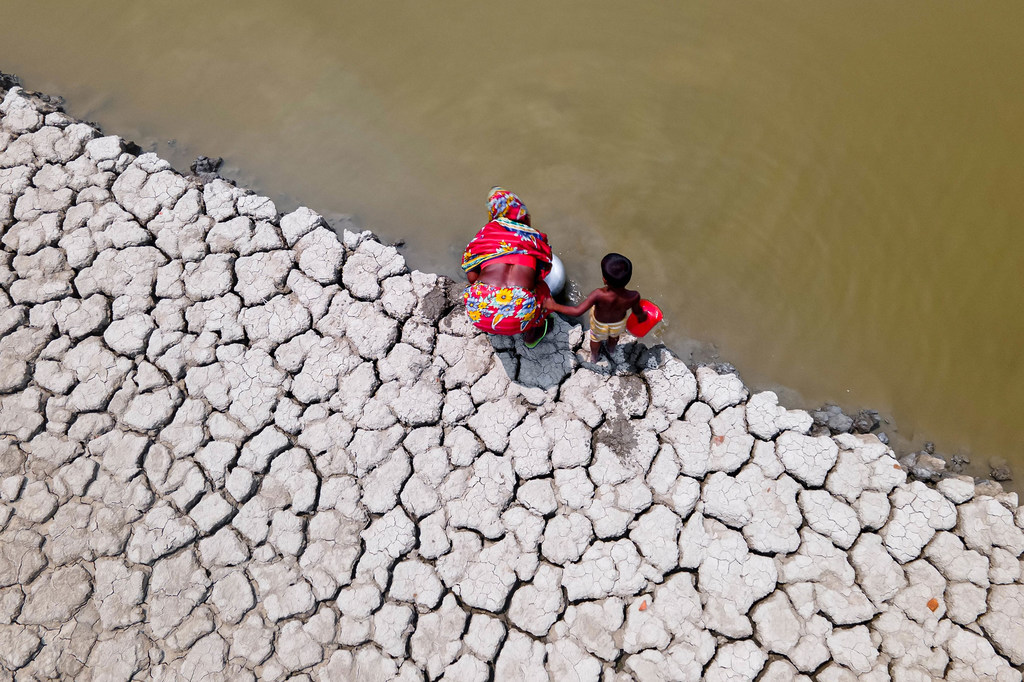 Dans la zone côtière de Shyamnagar, dans le district de Khulna au Bangladesh, une femme et son petit-fils recueillent l'eau laissée par la sécheresse pour l'utiliser.