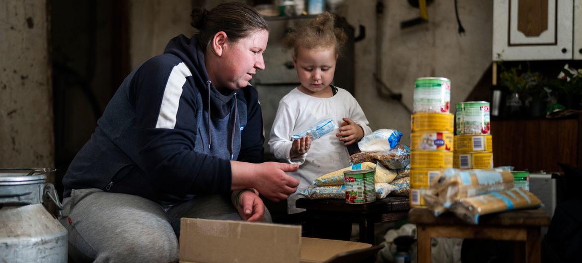 Une femme et un jeune enfant sont assis à une table avec des rations alimentaires provenant d'une boîte du PAM , dans un foyer ukrainien.
