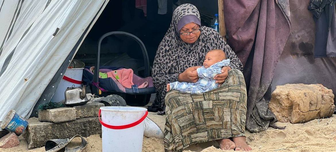 سيدة فلسطينية نازحة تحمل طفلا خارجة خيمة في قطاع غزة.