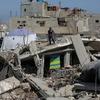 يقف رجل فلسطيني وسط أنقاض مبنى مدمر في خان يونس، غزة، مع وجود خيمة بيضاء منصوبة في الخلفية.