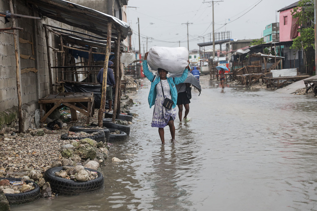 Una mujer camina por Les Cayes, en el sur de Haití, llevando consigo sus pertenencias mientras el agua de la inundación la rodea.