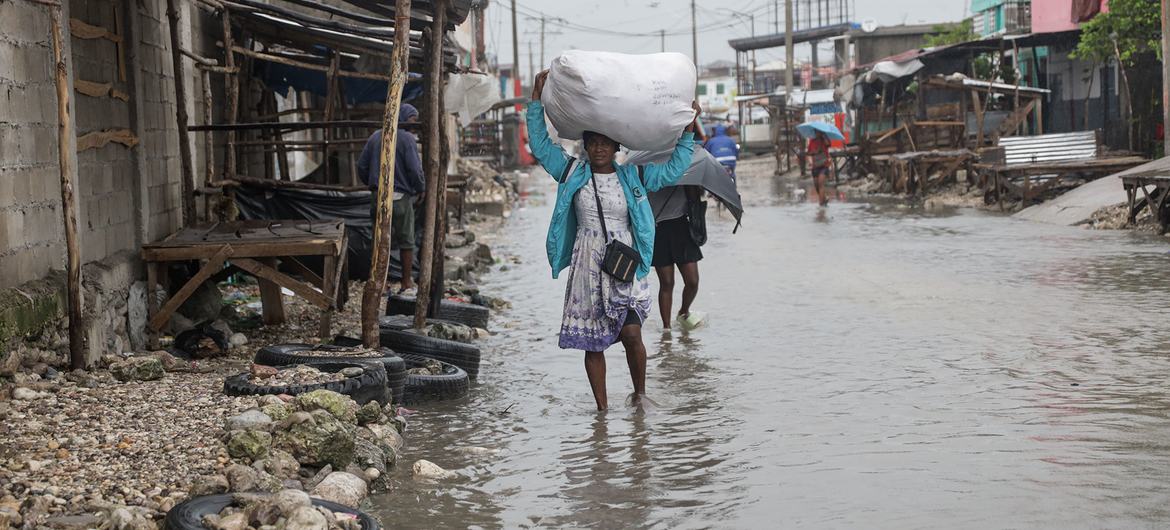 Una mujer camina por Les Cayes, en el sur de Haití, llevando consigo sus pertenencias mientras el agua de la inundación la rodea.
