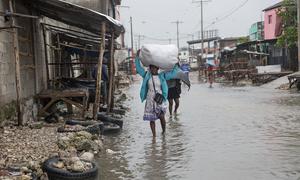 Una mujer camina por Les Cayes, en el sur de Haití, llevando consigo sus pertenencias mientras el agua de la inundación la rodea.