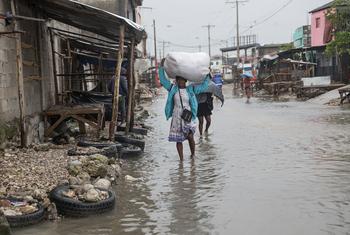 Una mujer camina por Les Cayes, en el sur de Haití, llevando consigo sus pertenencias mientras el agua de la inundación la rodea.