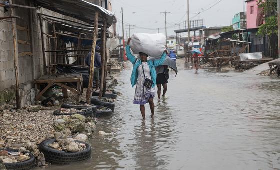 Una mujer camina por Les Cayes, en el sur de Haití, llevando consigo sus pertenencias mientras el agua de la inundación la rodea.