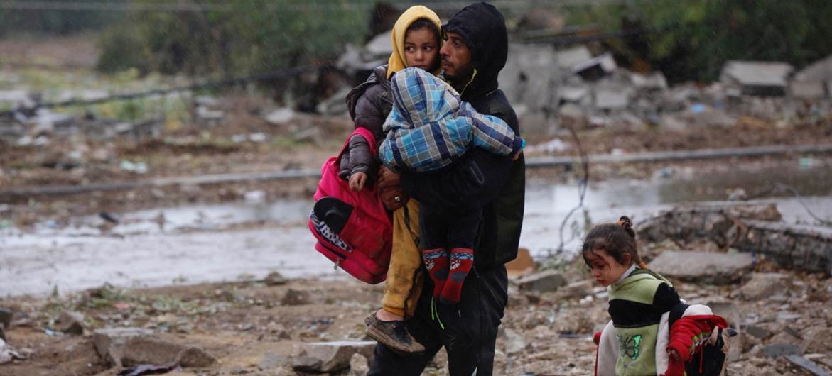 Um homem leva seus filhos por terras bombardeadas na Faixa de Gaza durante a pausa humanitária temporária