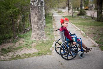 A young girl in a wheelchair moves along a path in Kyrgyzstan.
